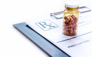 A new executive order aims to bring down the cost of prescription drugs and can impact Indiana Group Health Insurance image shows container of pills on clipboard